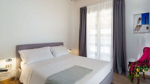 A bedroom with a bed, a nightstand, a chair, and a window with curtains. - Belvilla by OYO Villa Kika (Noto)