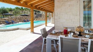 A covered outdoor area with a pool, lounge chairs, and a table set for dining. - Belvilla by OYO Villa Kika (Noto)