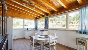 A kitchen with wooden beams, a dining table with chairs, a sink, and a window with curtains. - Belvilla by OYO Villa Kika (Noto)