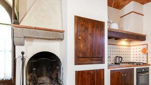 Eine Küche mit Kamin aus Stein, Holzschränken, einer gefliesten Rückwand und einem Gasherd.
