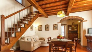 A spacious living area with a wooden staircase, a dining table with chairs, a sofa, and a kitchen area with a television. - Villa with Spacious Garden, Swimming Pool, Hot Tub, Tennis Court near Cortona (Cortona)
