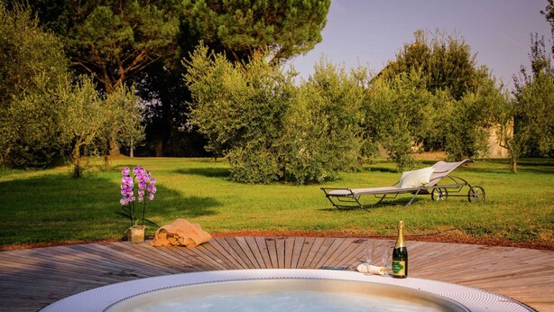 A hot tub surrounded by a wooden deck, with a lounge chair and a bottle of champagne nearby. - Villa with Spacious Garden, Swimming Pool, Hot Tub, Tennis Court near Cortona (Cortona)