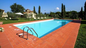 A rectangular swimming pool with a clear blue water surface, surrounded by a red brick deck. There are metal pool ladders on the left side, and a few lounge chairs are visible in the background. - Villa with Spacious Garden, Swimming Pool, Hot Tub, Tennis Court near Cortona (Cortona)