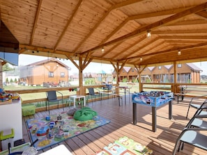 A covered outdoor area with wooden flooring, tables, chairs, and a foosball table.