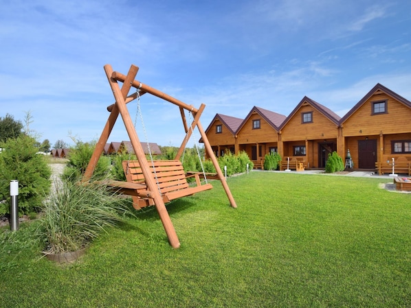 A wooden swing set in a grassy area with a row of log cabins in the background.