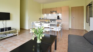 A modern living room with a flat-screen TV, a coffee table with a vase of flowers, and a grey sofa. - Quaint Apartment in Zierow near Sea (Zierow)