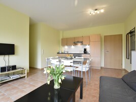 Una sala de estar moderna con un televisor de pantalla plana, una mesa de centro con un jarrón de flores y un sofá gris.