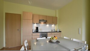 A modern kitchen with wooden cabinets, a stainless steel stove, and a dining table with a fruit bowl. - Quaint Apartment in Zierow near Sea (Zierow)