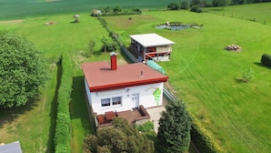 A large house with a red roof, surrounded by a well-maintained lawn and a small pond.