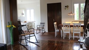 Un comedor amplio con suelo de madera, sillas blancas y una mesa central.