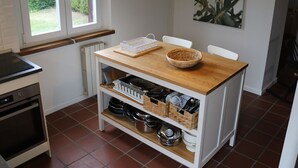 Una cocina con una mesa de madera, sillas blancas, una lámpara colgante y un ventanal con vistas a zonas verdes.