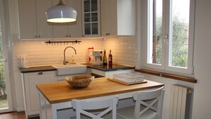 Cocina con armarios blancos, encimera de madera, lámpara colgante y ventana con vistas al verdor.