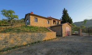 A stone building with a small attached structure, a gravel driveway, and a metal gate.