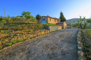 A stone house with a gravel driveway leading to a gated entrance.