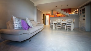 Un salon moderne comprenant un canapé, une table à manger et des chaises. Il y a également un coin cuisine et un escalier menant à l’étage supérieur.