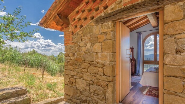 Un edificio in pietra con tetto in legno, un ingresso che conduce a una camera da letto con un letto e vista sulle montagne.