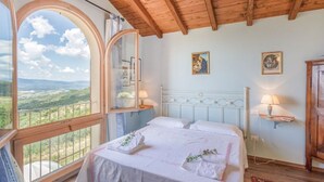 Una camera da letto con un'ampia finestra ad arco, un letto con lenzuola bianche e un soffitto in legno.