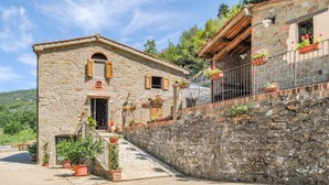 Un edificio in pietra con una porta di legno e persiane, circondato da piante in vaso e un muro in pietra.