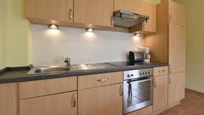 A modern kitchen with wooden cabinets, stainless steel appliances, and a built-in oven. - Gemutliches Appartement in Zierow mit Aussenkamin (Zierow)