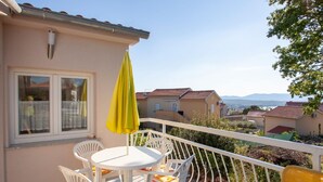 A balcony with a table and chairs, a yellow umbrella, and a view of the surrounding neighborhood. - Apartment in Sveti Vid Near the Adriatic (Malinska-Dubasnica)