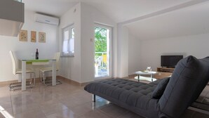 A modern living room with a grey sofa, a dining table with chairs, a TV, and a balcony with a view of greenery. - Apartment in Sveti Vid Near the Adriatic (Malinska-Dubasnica)