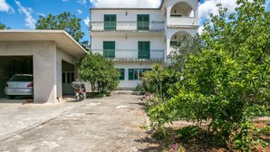 Un bâtiment à deux étages avec un garage, un scooter garé et un jardin où poussent différentes plantes.