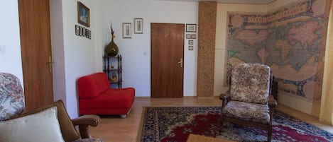 A living room with a wooden floor, a red sofa, a patterned armchair, a coffee table, and a map on the wall.