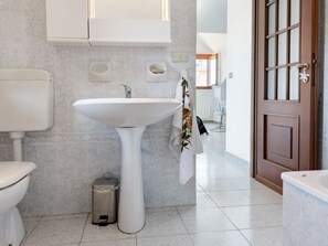 A modern bathroom with a pedestal sink, toilet, and trash can. - Apartment in Cassinelle With Garden & BBQ (Cassinelle)