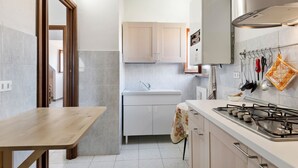 A compact kitchen with a wooden table, white cabinets, a gas stove, and a hanging pot rack. - Apartment in Cassinelle With Garden & BBQ (Cassinelle)