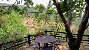 A stone patio with a round table and chairs, surrounded by a wooden fence and trees. - Cottage in Cortona With Pool & Stunning Views (Cortona)
