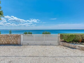 A coastal view with a stone wall and a white gate leading to a gravel path.
