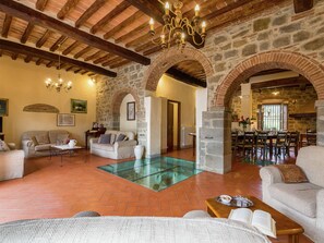 A spacious living area with a glass coffee table, sofas, and a dining area with wooden chairs and a table.