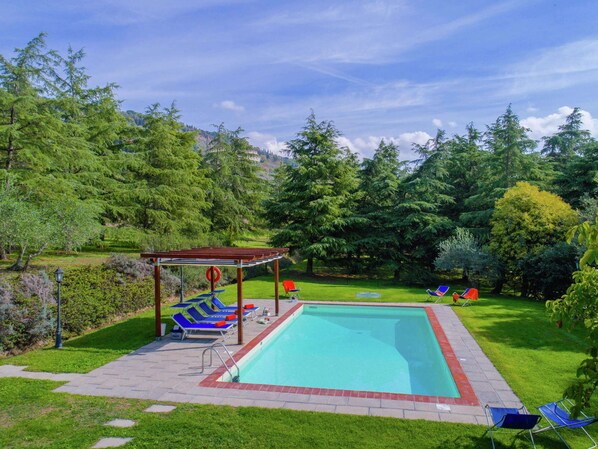A rectangular swimming pool with a wooden pergola and lounge chairs.