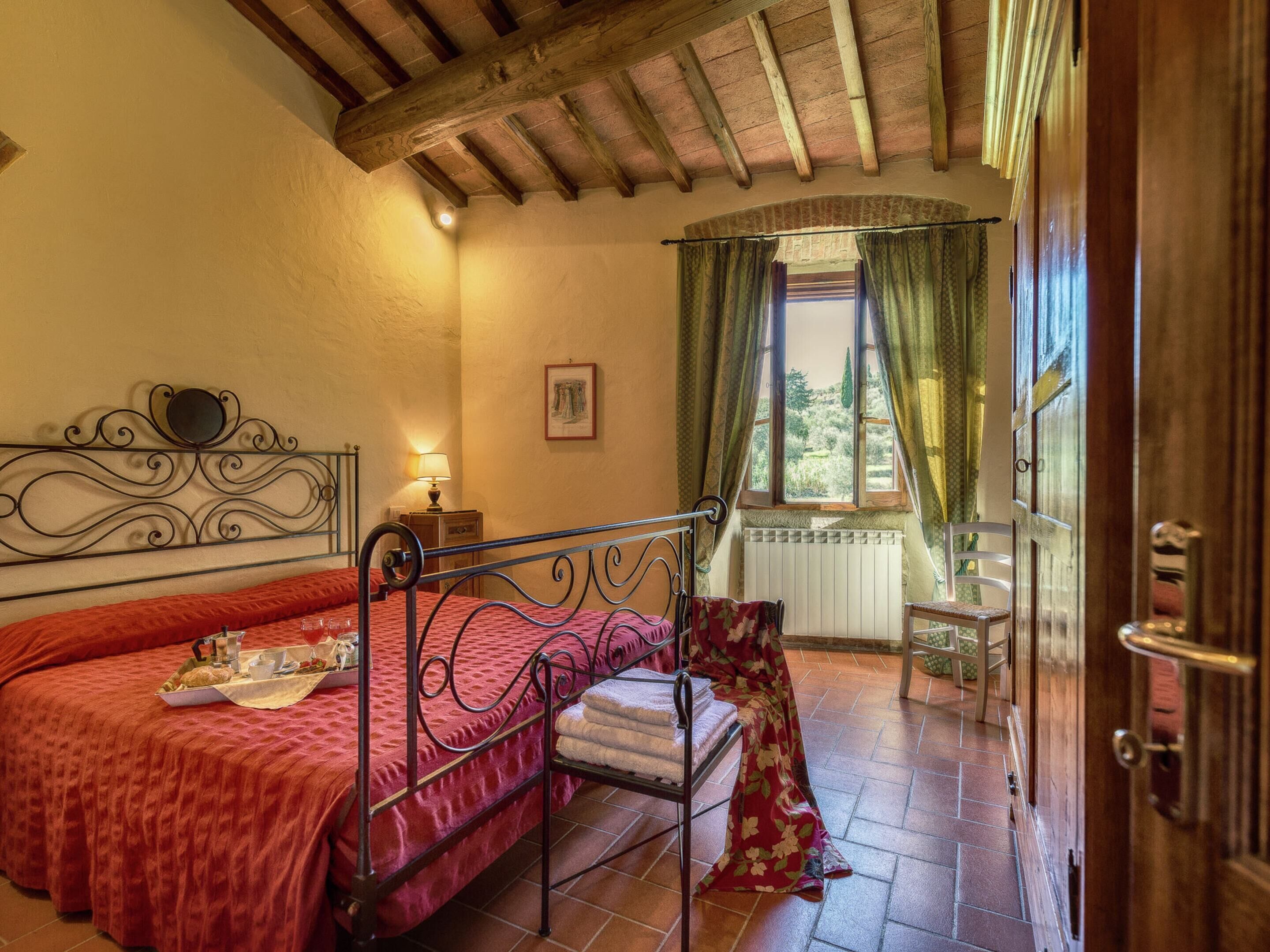 Un dormitorio con cama, mesita de noche, lámpara, ventana con cortinas y vistas al exterior.