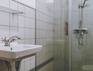 Un baño con un lavamanos blanco, una ducha con cabezal de ducha manual y paredes cubiertas de azulejos.