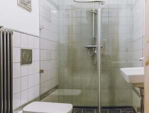 Un baño con ducha envuelta en vidrio, inodoro y lavamanos.
