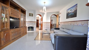 A spacious living room with a large wooden cabinet, a flat-screen TV, a fireplace, a sofa, and a patterned wall. - Villa in Typical Portuguese Style, Quiet Area of Vilamoura With Private Pool (Loulé)