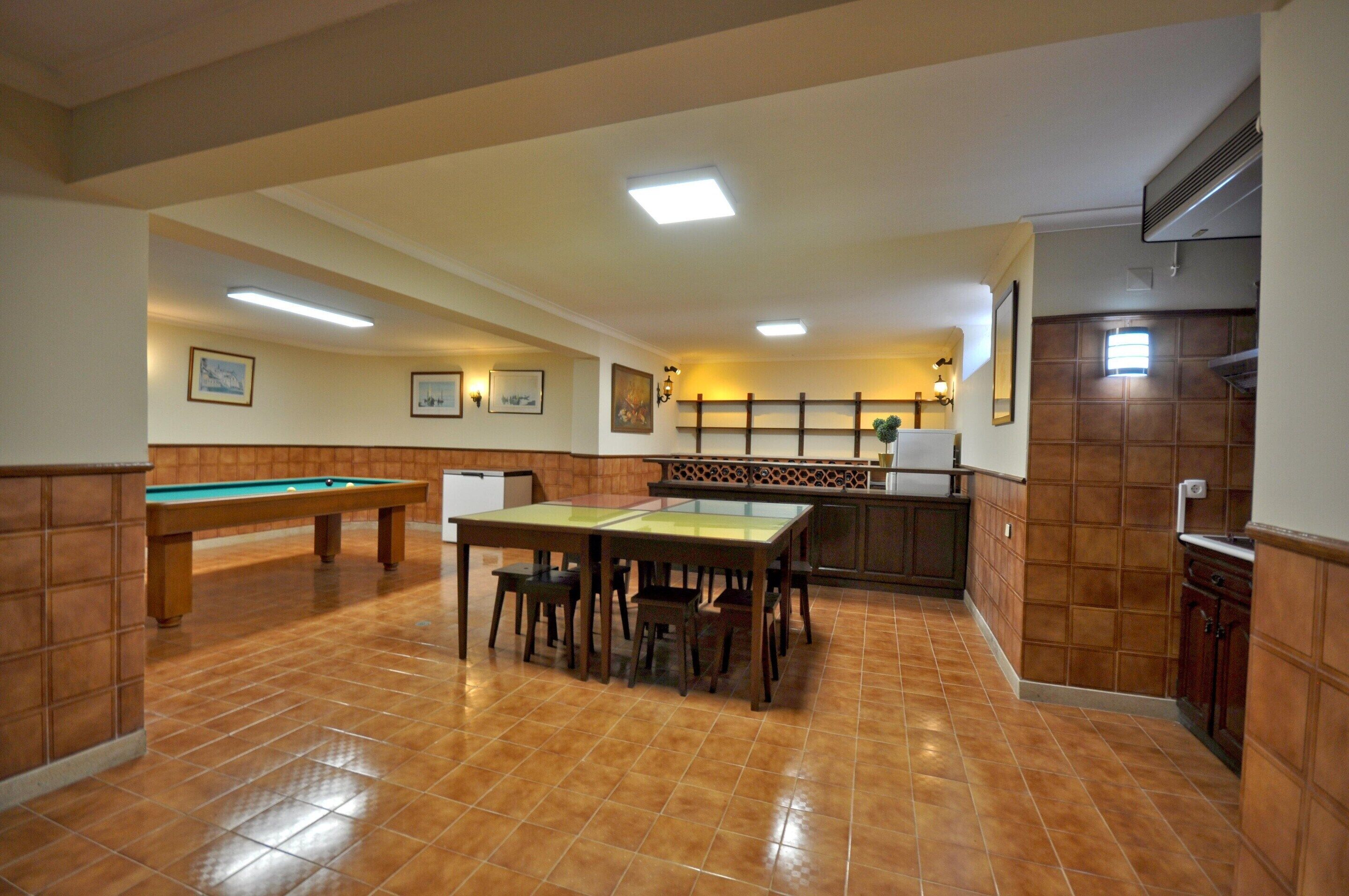 A spacious room with a pool table, a dining table with chairs, and a kitchen area with a sink and cabinets.