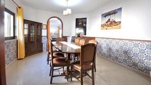 A dining area with a large wooden table, six chairs, a chandelier, and a tiled backsplash. - Villa in Typical Portuguese Style, Quiet Area of Vilamoura With Private Pool (Loulé)