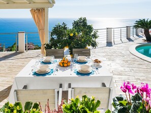 A table set for four with a view of the sea, a pool, and a wooden deck. - Villa With Panoramic Sea View Pool Near Taormina (Letojanni)