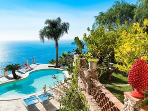 A swimming pool with lounge chairs, a palm tree, and a view of the ocean. - Villa With Panoramic Sea View Pool Near Taormina (Letojanni)