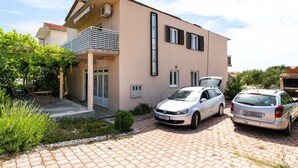 Un edificio di due piani con un balcone, un'auto parcheggiata davanti e un vialetto lastricato.