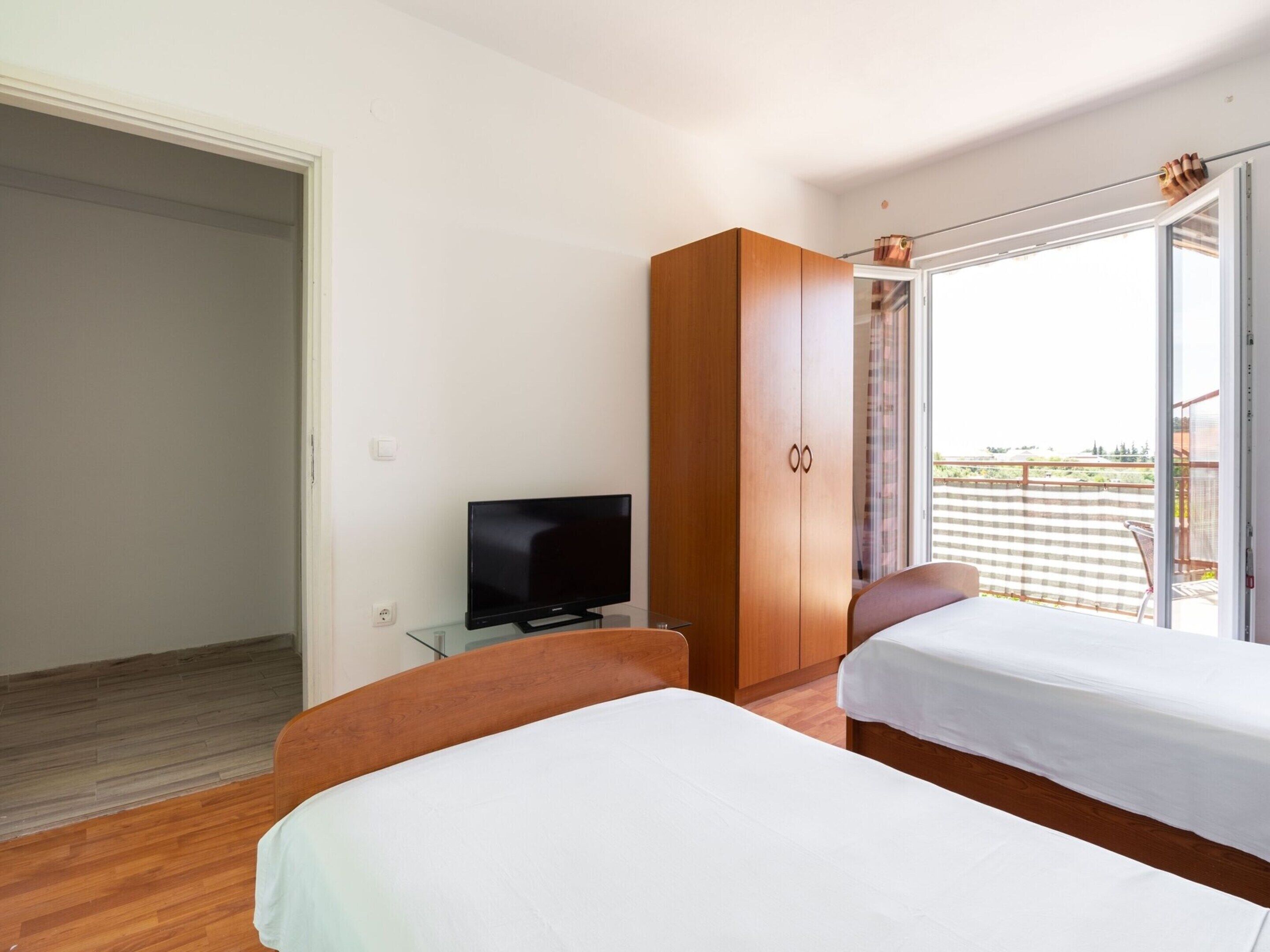 A hotel room with two beds, a TV, a wardrobe, and a balcony with a view.