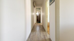 Un corridoio stretto con pavimento in legno, pareti bianche e una porta che dà su un bagno.