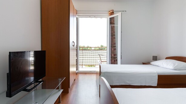 Una moderna camera d'hotel con una TV a schermo piatto, un tavolino in vetro, due letti, un armadio in legno e un balcone con vista.