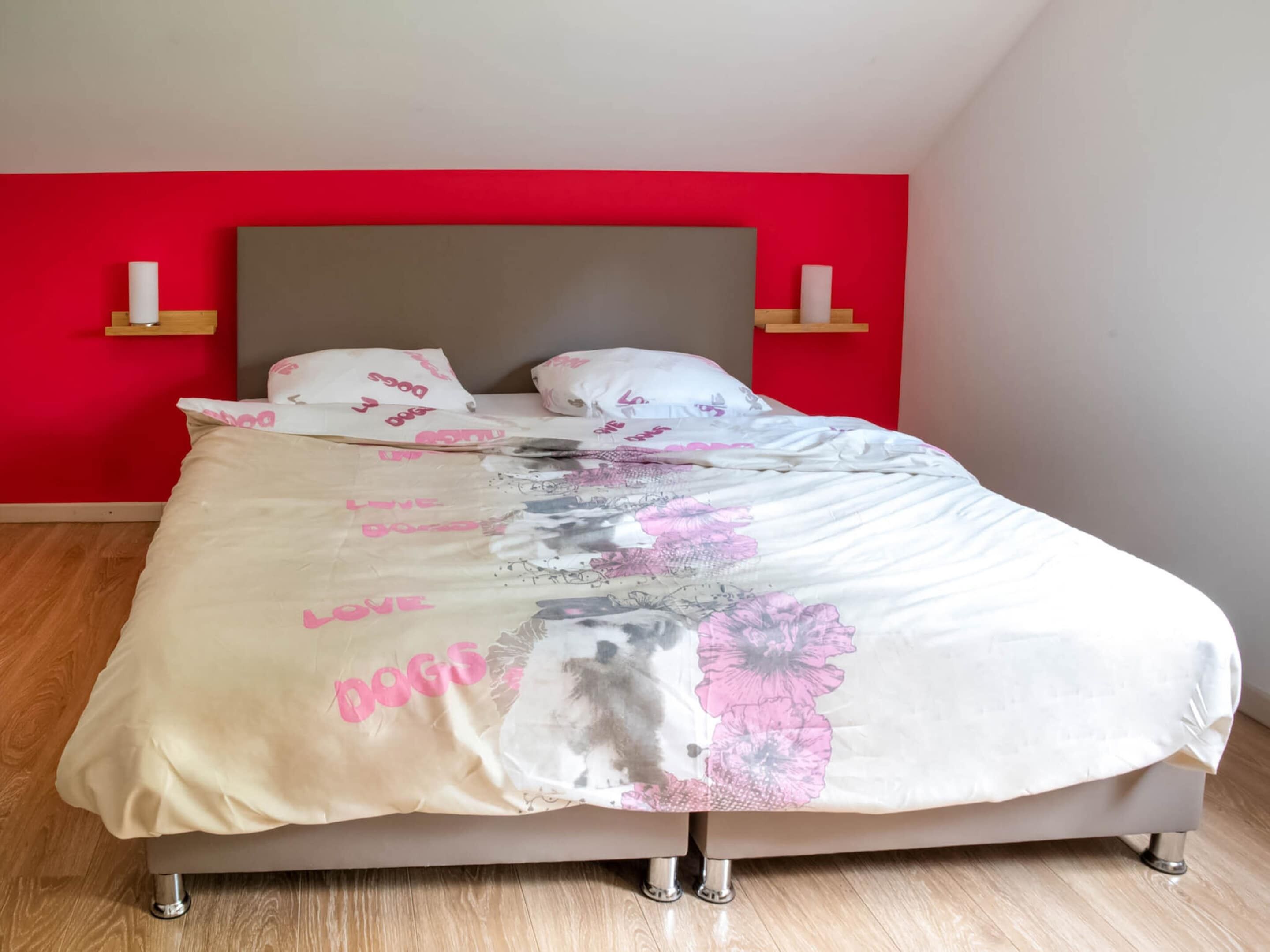 Ein Bett mit Blumenmuster auf der Bettdecke, eine rote Akzentwand und zwei Nachttische mit Kerzen.