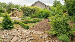 A garden with a wooden play structure, a stone pathway, and a house in the background. - Pleasant Holiday Home With Infrared Sauna (Durbuy)