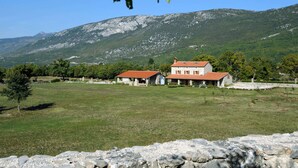 A stone house with a red roof in a rural setting, surrounded by a stone wall and a grassy field, with a mountain in the background. - Picturesque Mansion in Kozljak (Krsan)