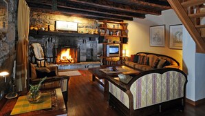 A cozy living room with a stone fireplace, wooden bookshelves, a comfortable sofa, and a wooden staircase. - Picturesque Mansion in Kozljak (Krsan)