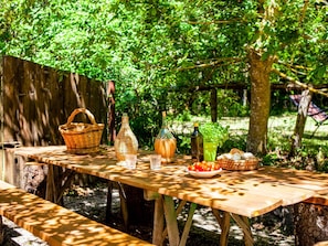 Ein Holztisch mit Picknickdecke im Freien, bestehend aus einem Korb, einer Flasche, einem Glas und einer Schüssel mit Tomaten.